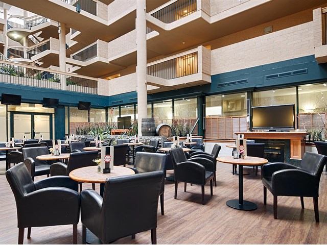 Hotel atrium dining area with round tables, black chairs, and modern decor.