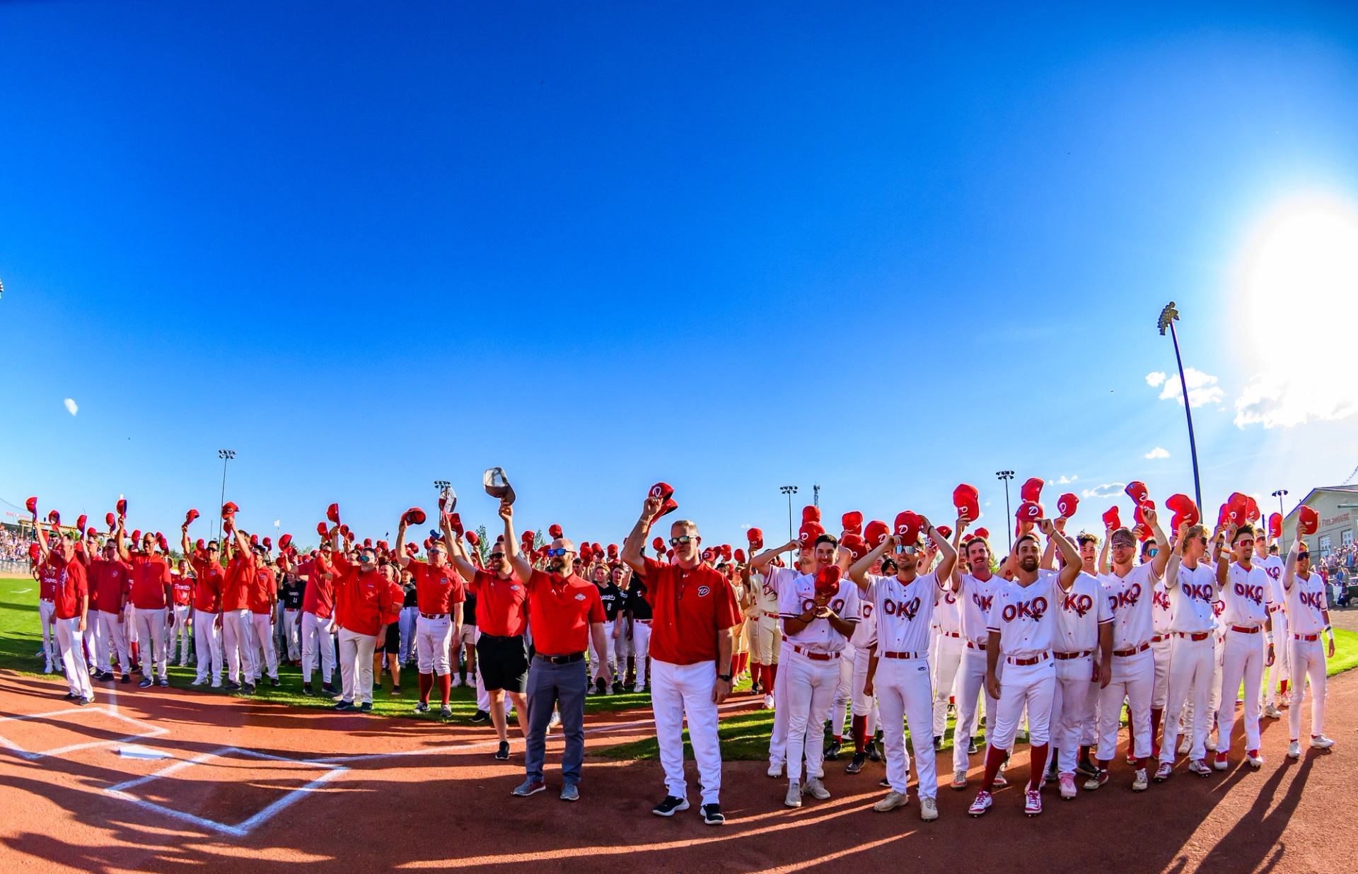 Baseball team in red and white uniforms lined up on the field under a clear blue sky.