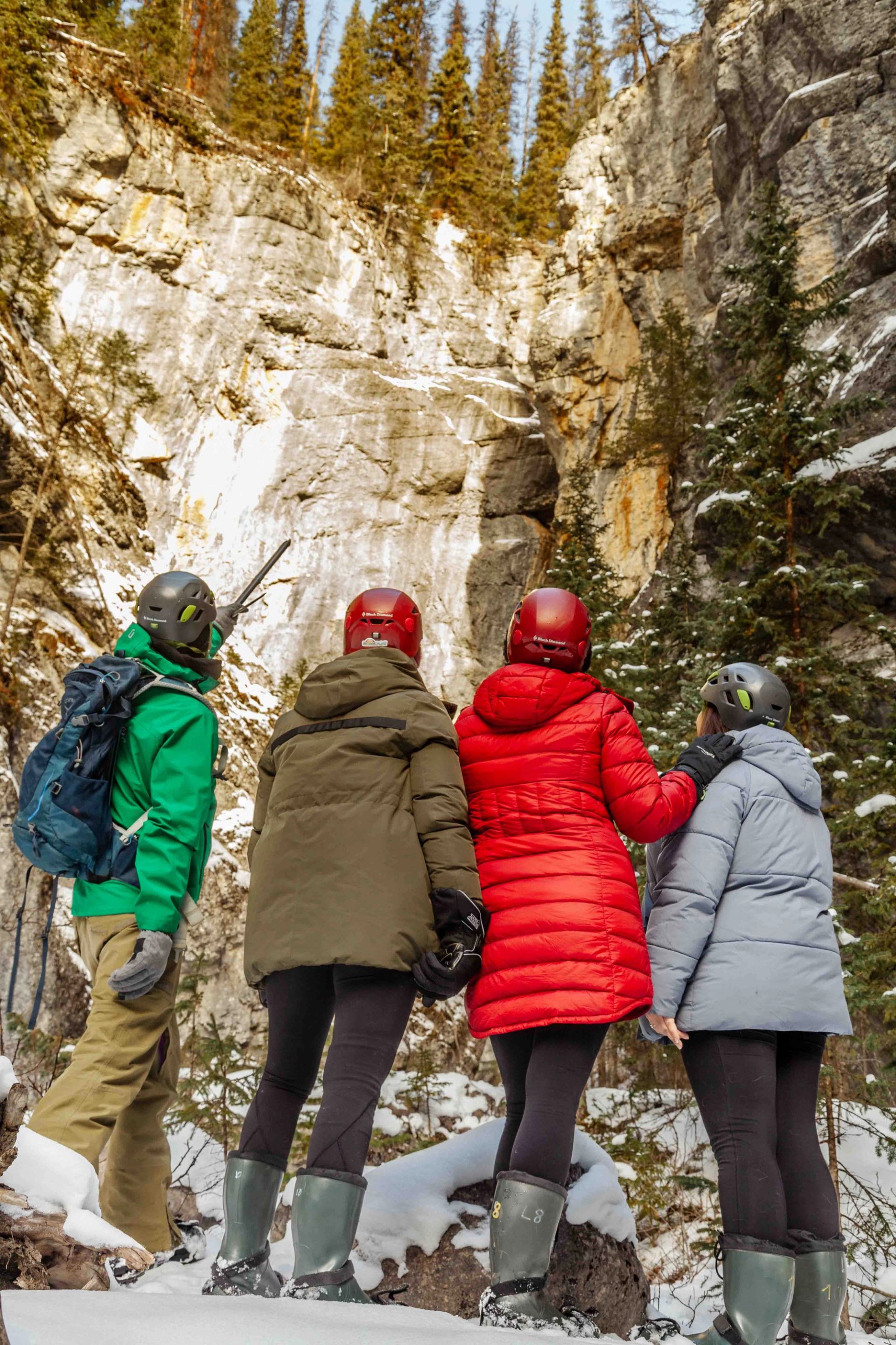 Four people in winter gear looking at a frozen waterfall in Maligne Canyon