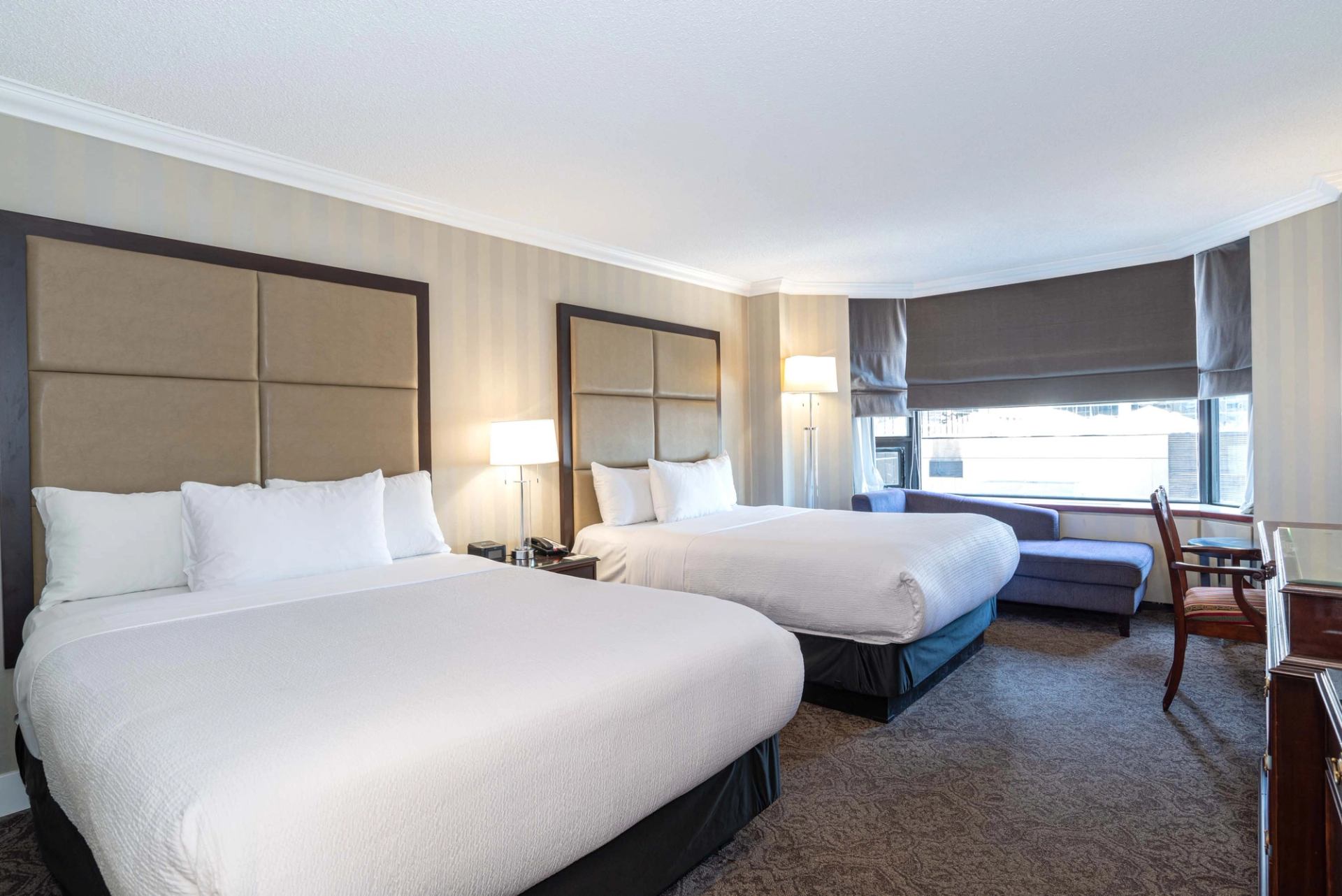Hotel room with two large beds, lamps, window seating area and desk.
