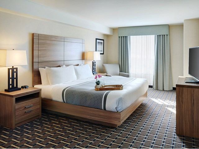 Spacious hotel room with a king bed, wooden furniture, and soft natural light