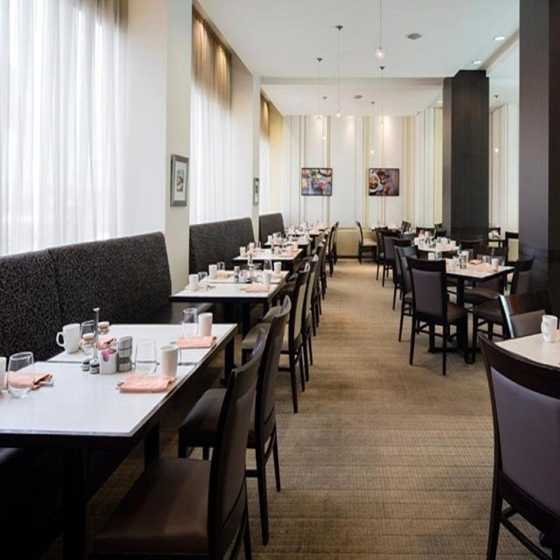 An unoccupied restaurant dining room with rows of set tables, booth seating, and individual chairs.