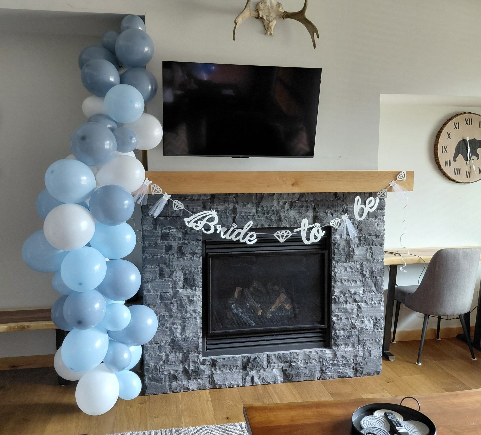 Blue and white balloon garland beside a stone fireplace with bride-to-be banner.