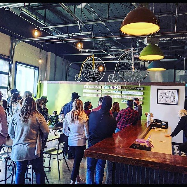 Tour group stands in a brewery near a bar counter, with bicycles on display.