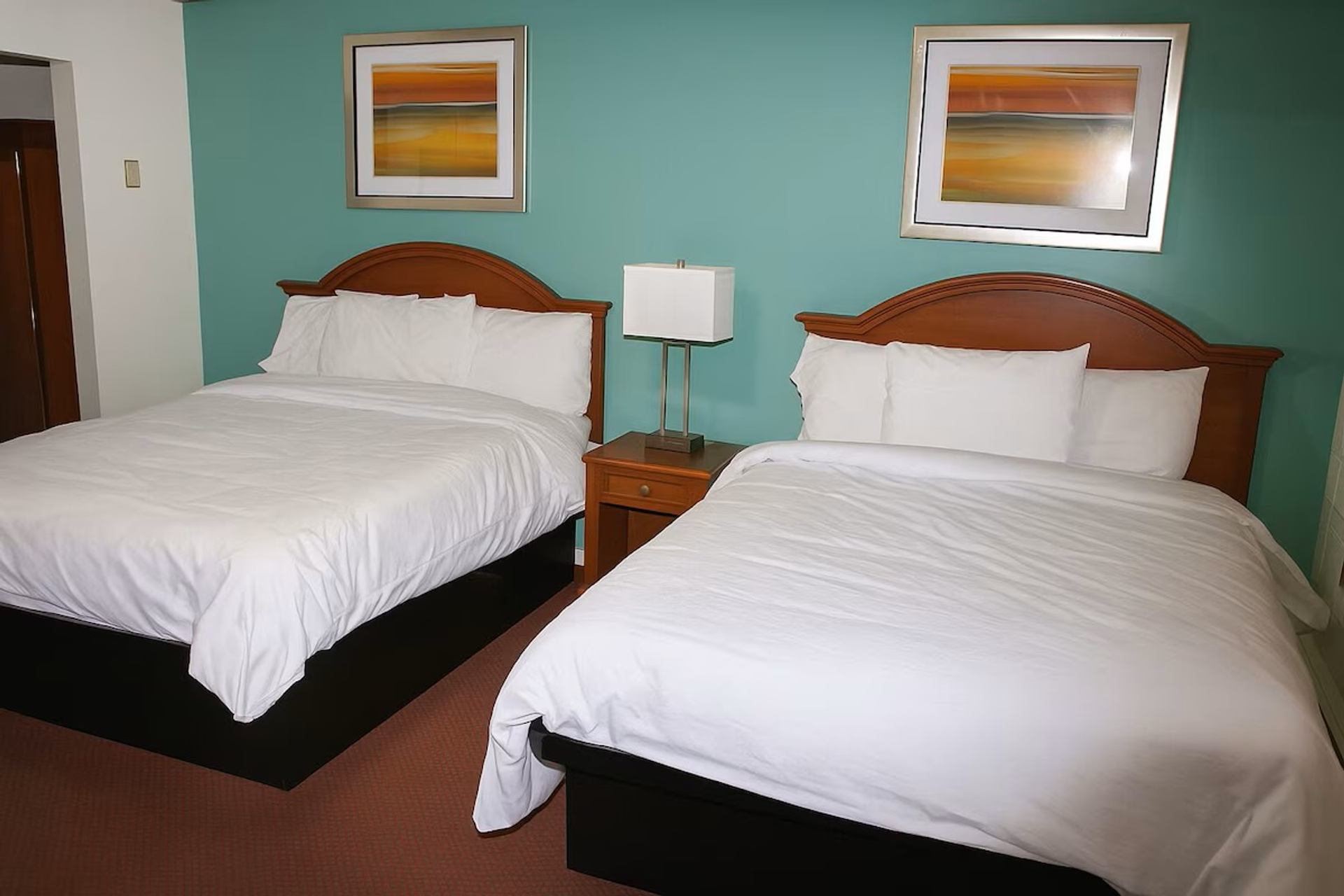 Hotel room with two white beds, teal wall, nightstand and framed abstract art.