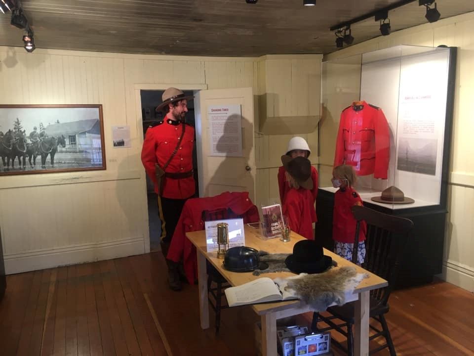 A man in RCMP uniform stands in a museum room with children exploring Mountie artifacts and uniforms.