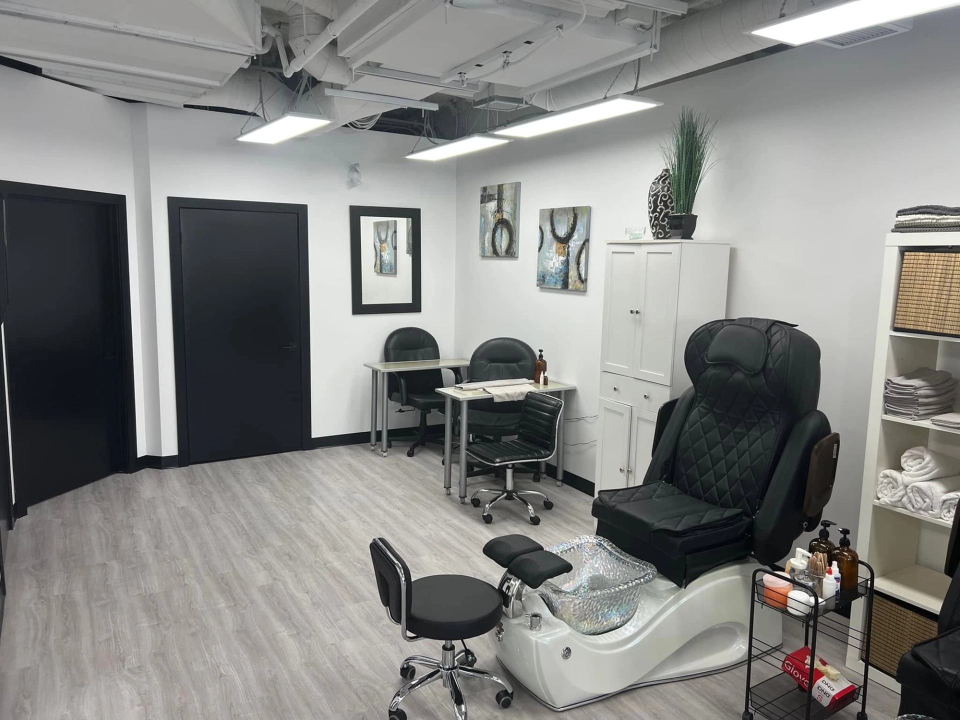Modern pedicure station with black massage chair, nail desks, cabinets and wall art.