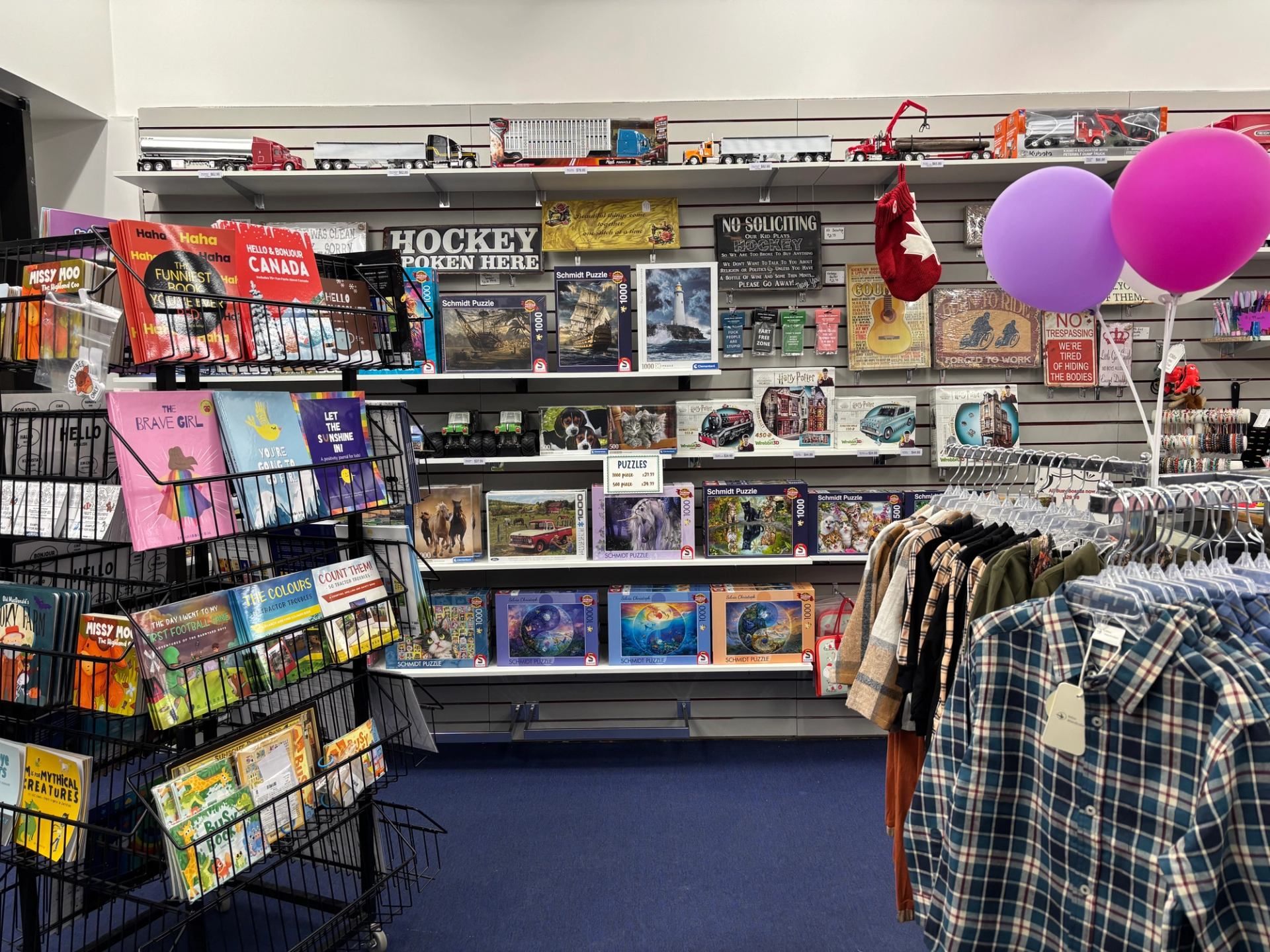 Children’s retail space with books, puzzles, toys, and clothing displayed on shelves and racks, with balloons above.
