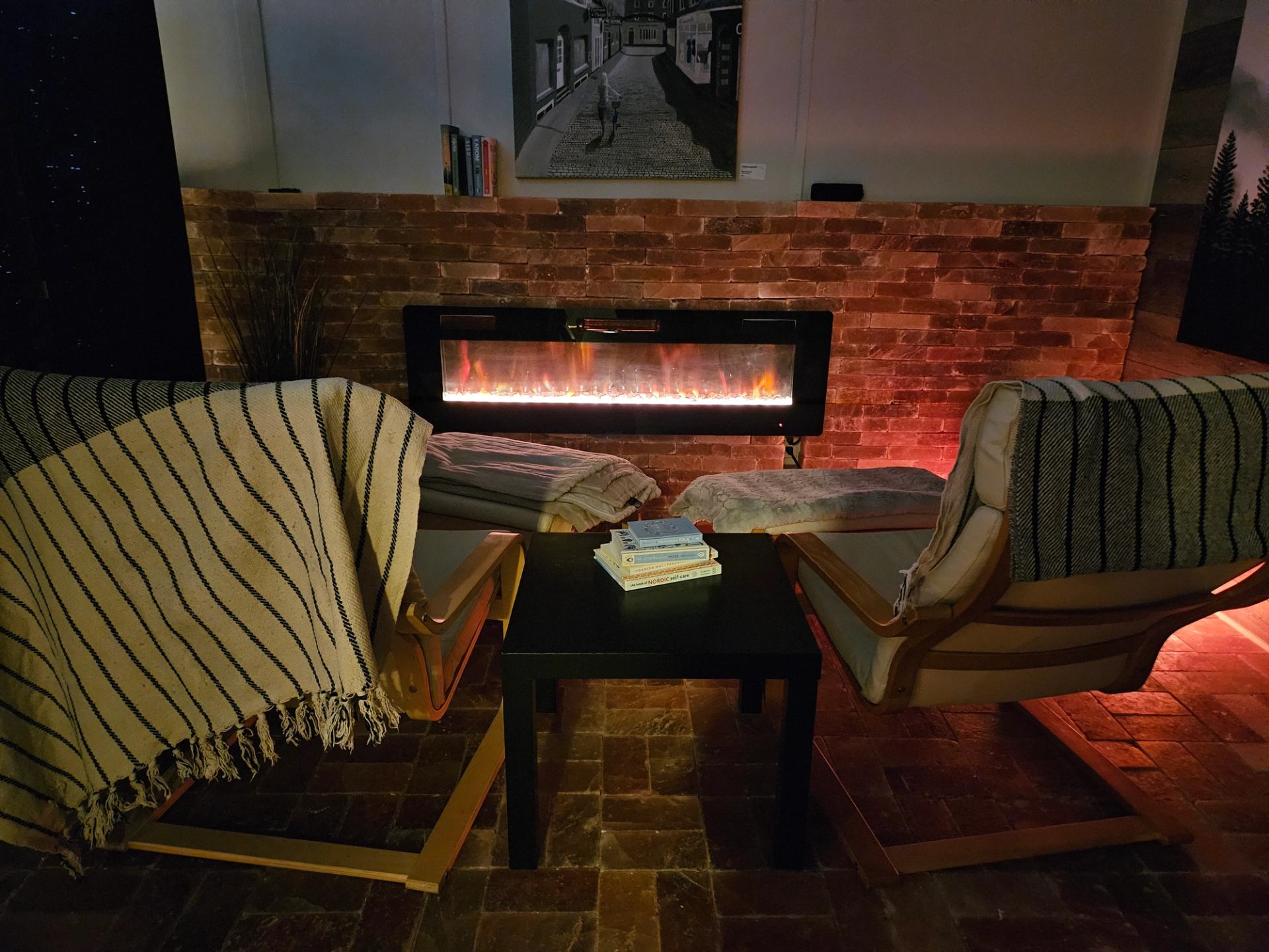 Cozy lounge with armchairs, books, and a glowing fireplace.