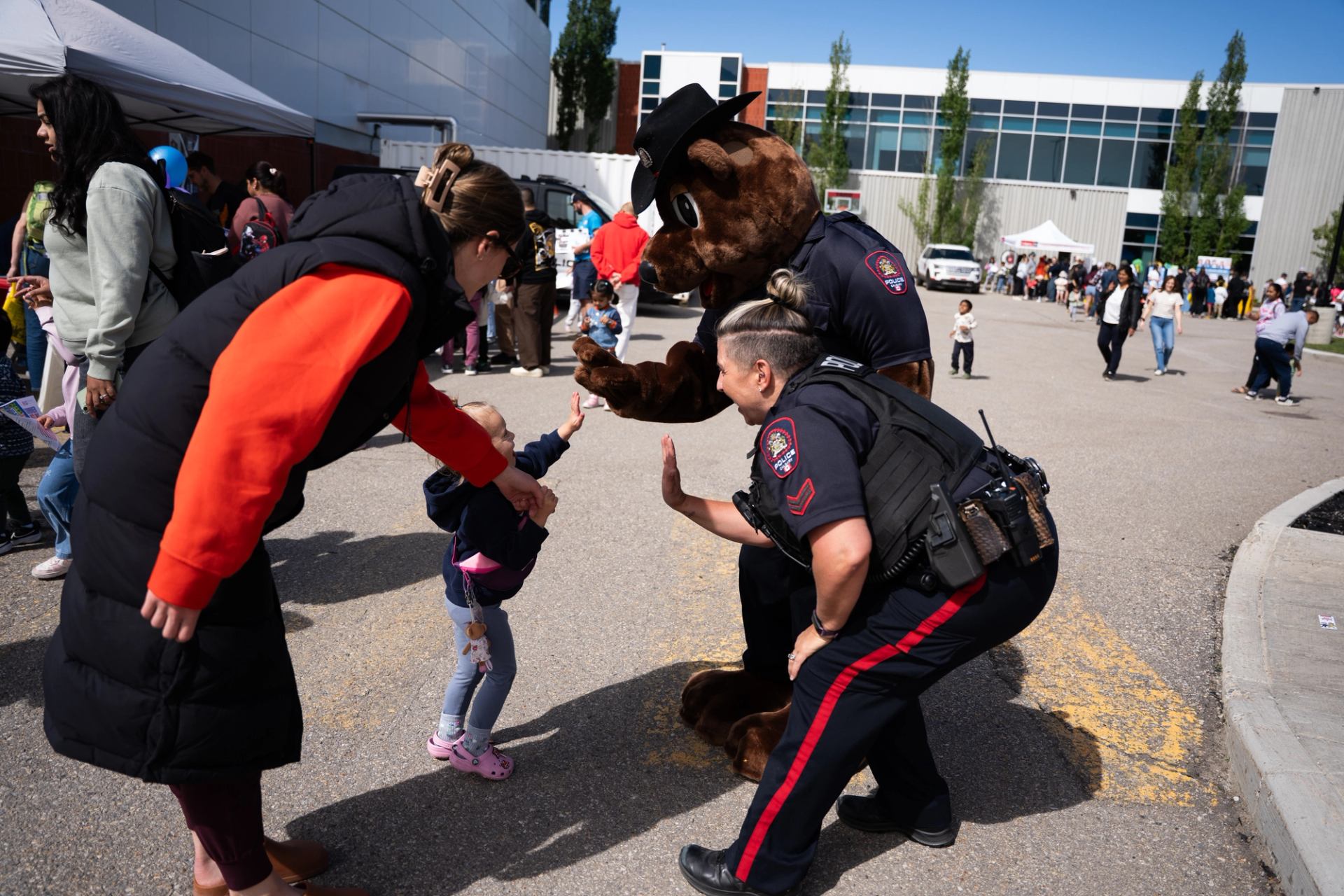 Child high-fives a police officer beside a bear mascot at an outdoor event.
