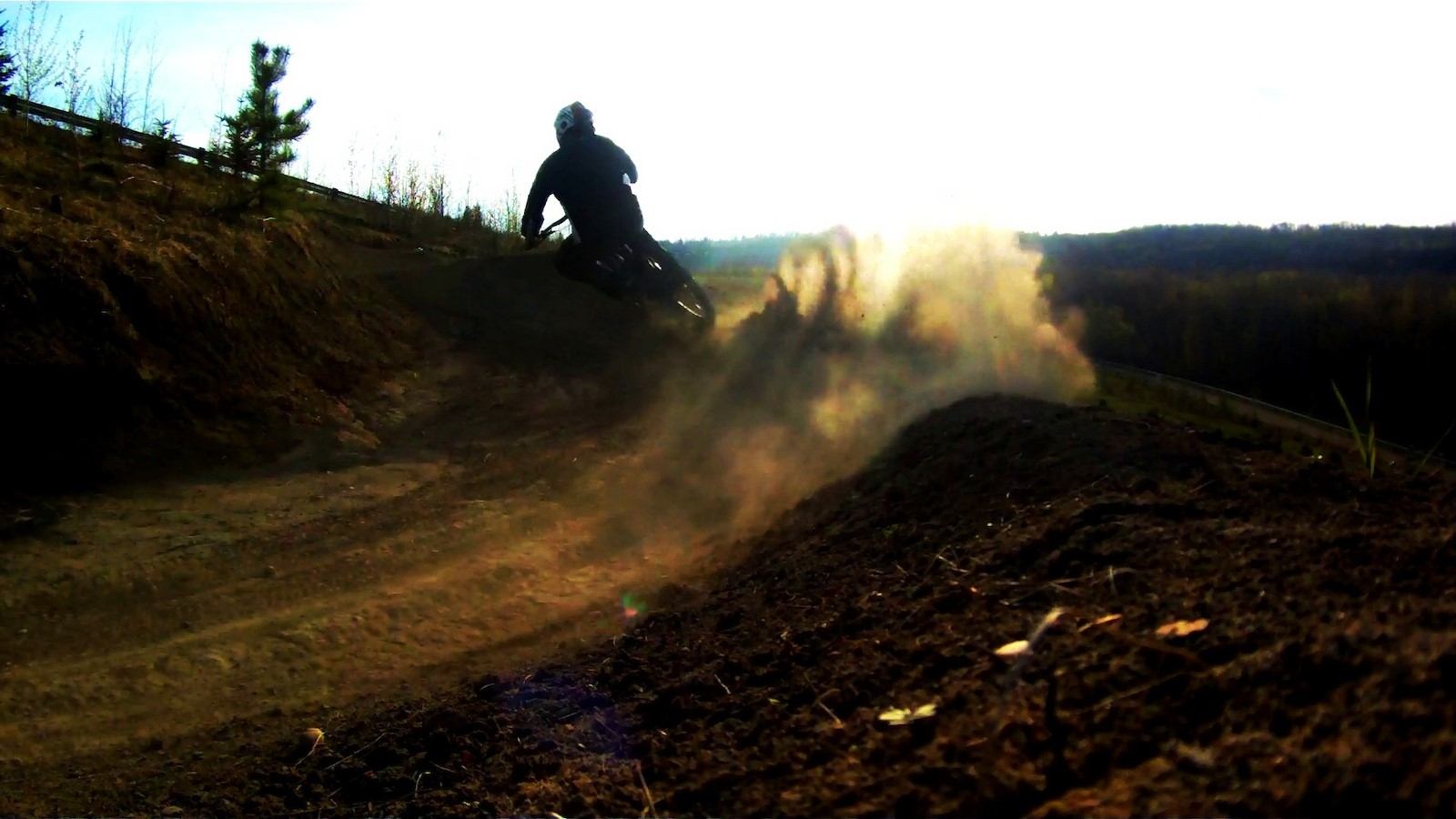 Cyclist rides a dirt berm, kicking up dust on a trail.