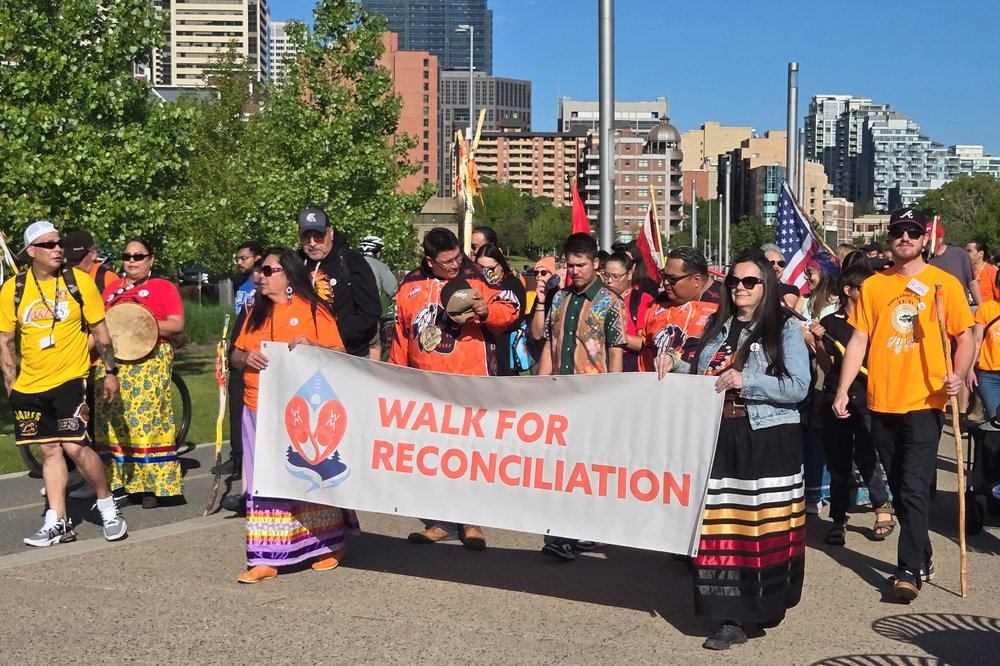 Crowd marching with a banner reading “Walk for Reconciliation” in downtown Calgary park.