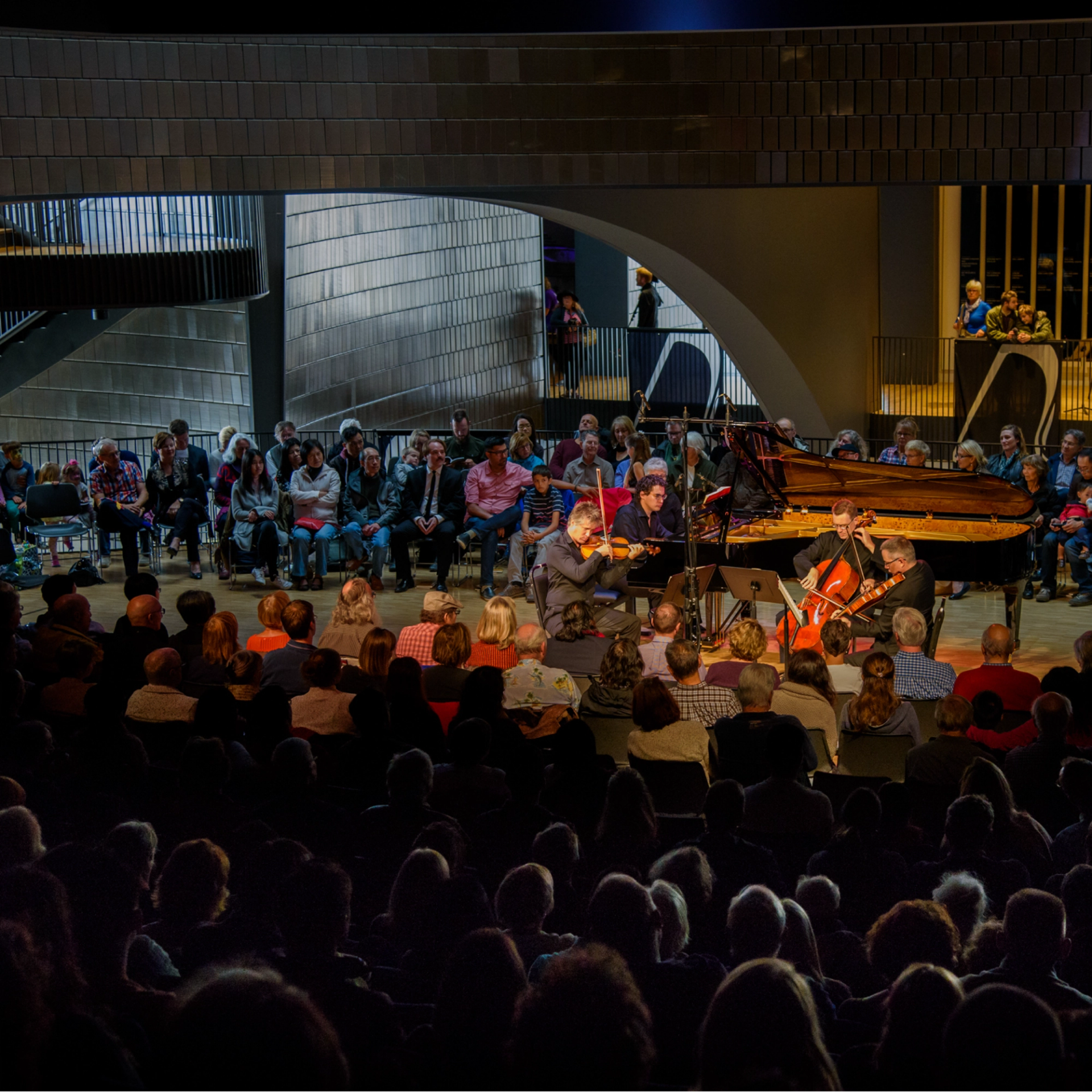 Musicians perform on stage in a concert hall with a seated audience.