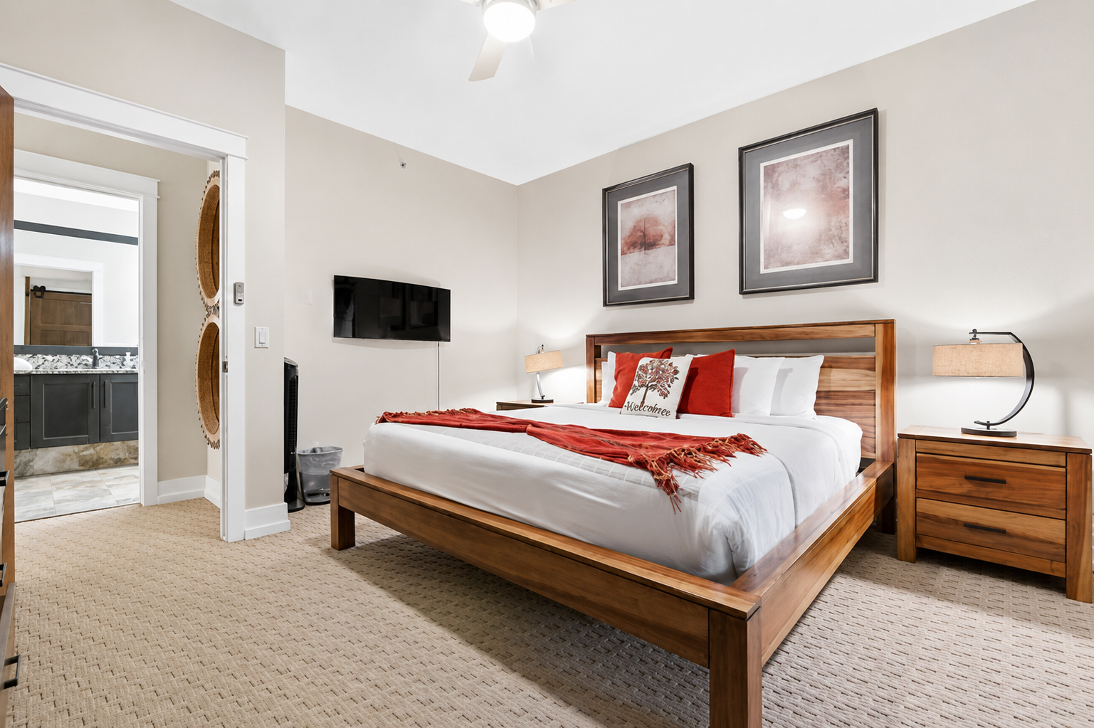 Bedroom with wooden bed, red accents, bedside tables and wall-mounted television.