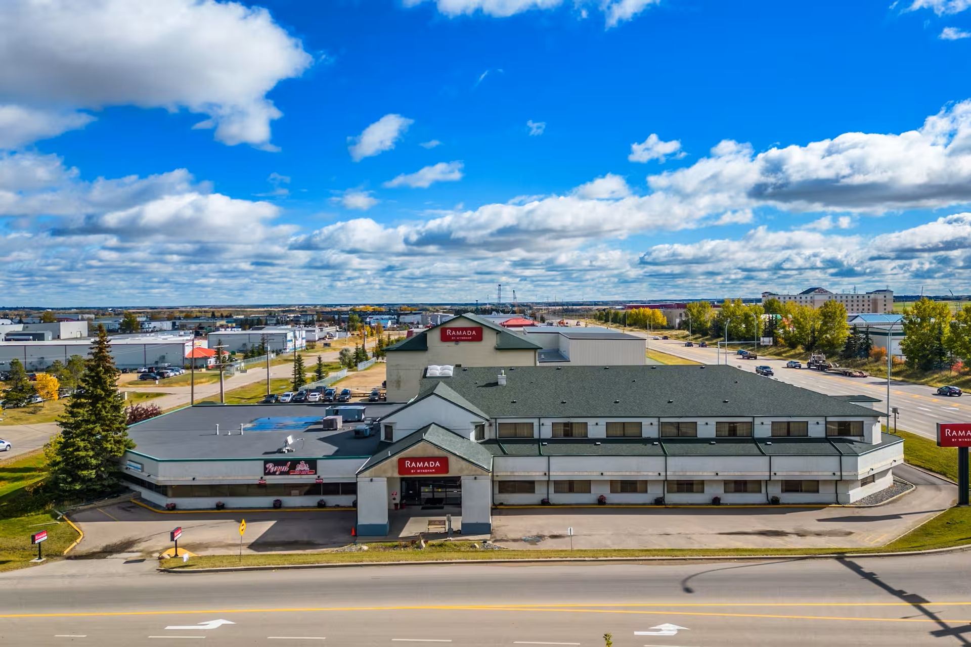 Exterior view of Ramada by Wyndham Nisku beside a roadway under a bright blue sky.