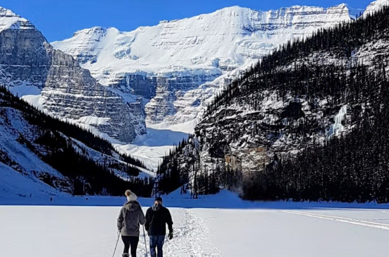 Two people walking on a snowy trail with towering mountains in the background at Rocky Mountain Couples Retreat.