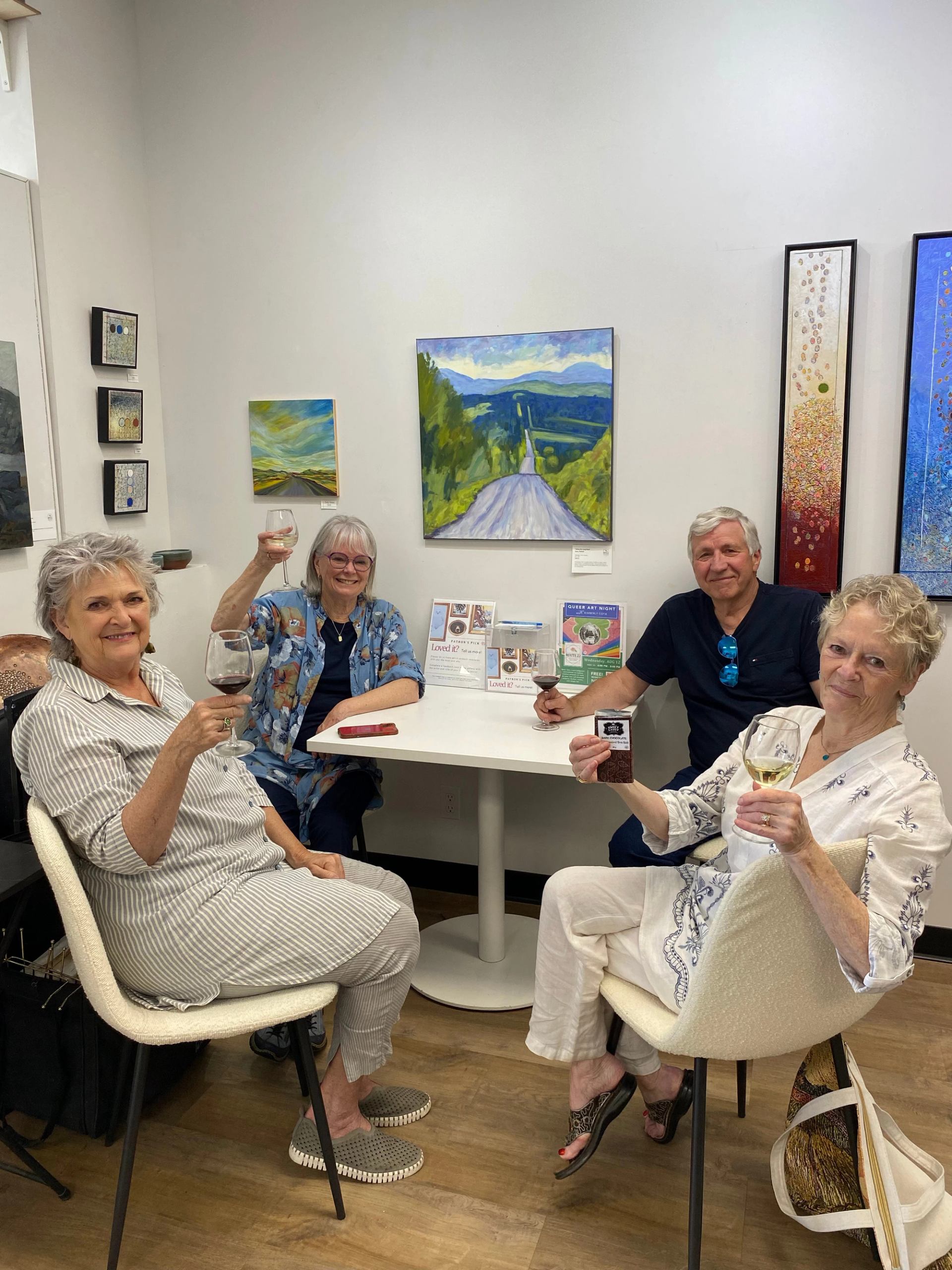 Four people raise wine glasses around a table in an art gallery.