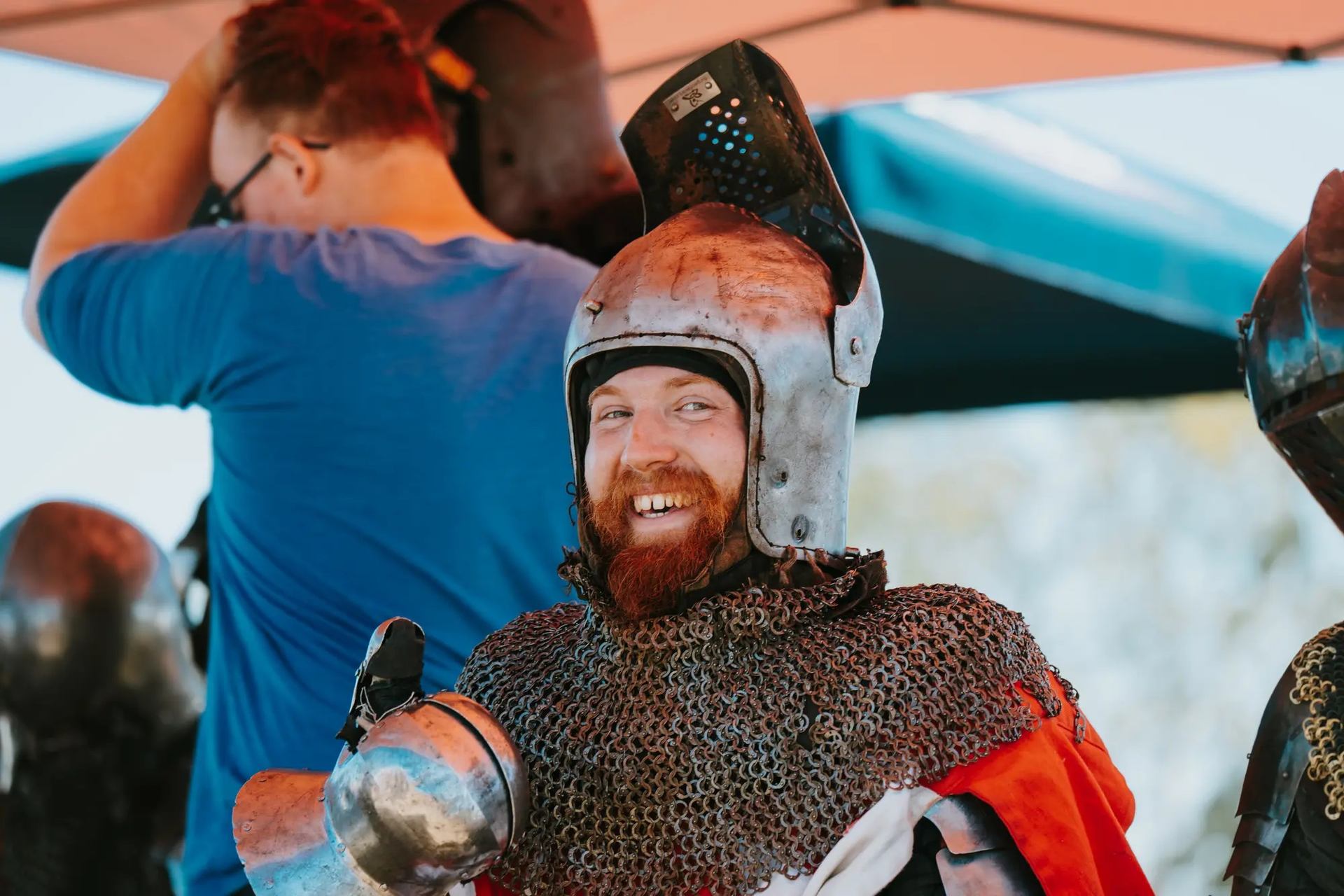 Person in medieval armor smiling under a tent at a historical reenactment event.