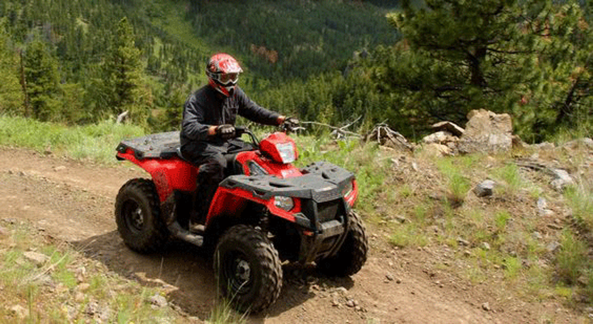 Red ATV navigating a dirt trail surrounded by green trees and hills