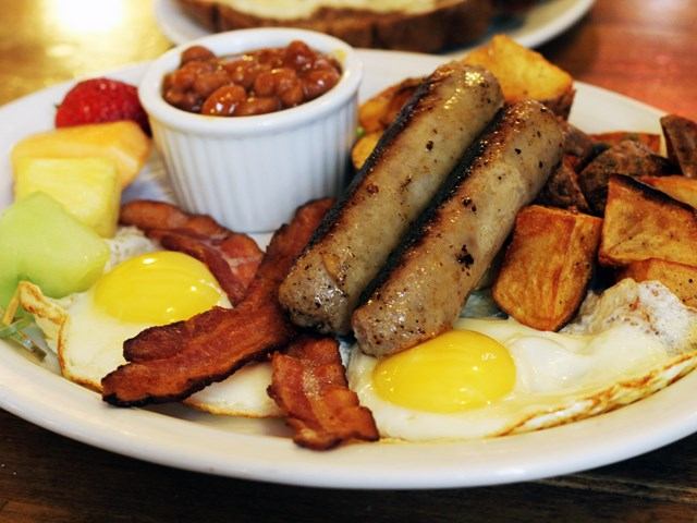 Hearty breakfast with eggs, bacon, sausage, potatoes, beans, and fruit.