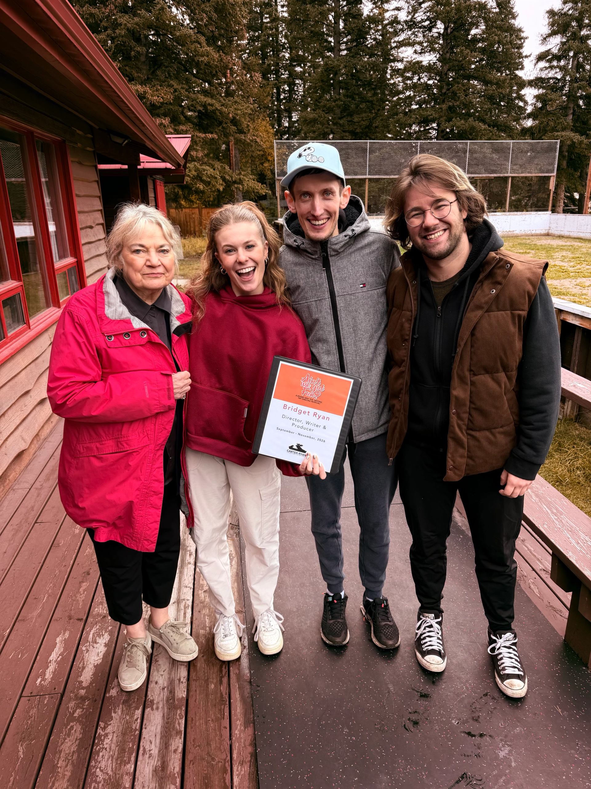 Four people pose on a wooden deck, with one holding a production binder.