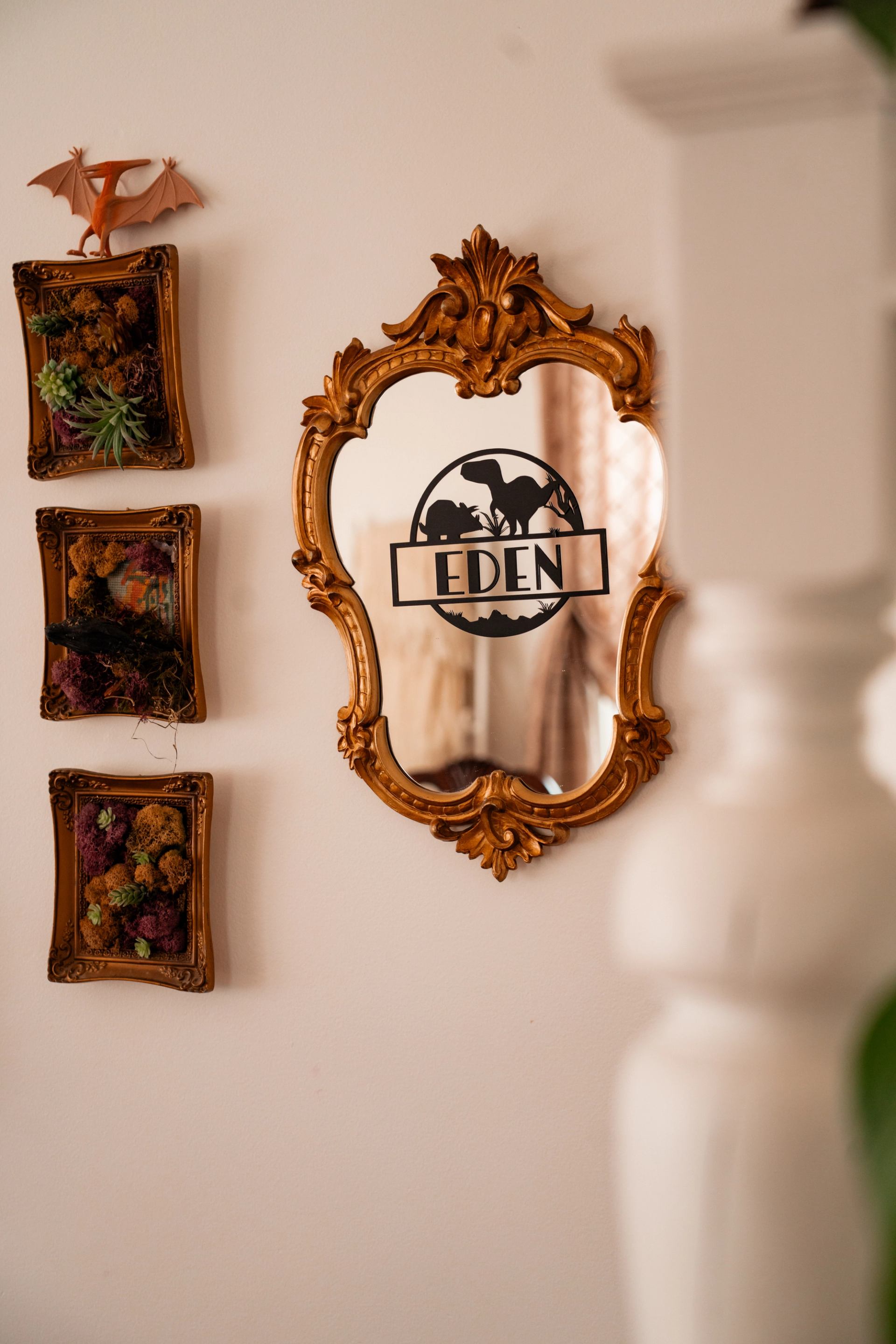 From the business's view, an ornate gold-framed mirror hangs beside botanical wall art on a bright wall.