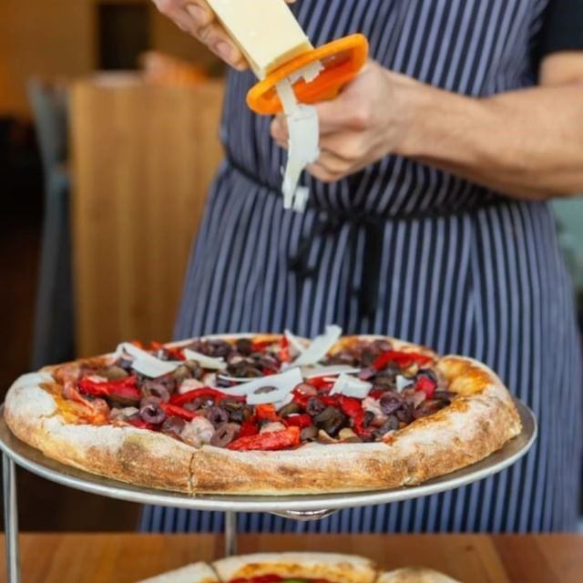Pizza on metal tray, server holds bottle above with red and white toppings.