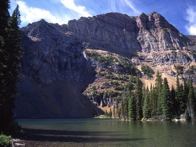 Tranquil Goat Lake with forested shores and rocky cliffs under a blue sky.
