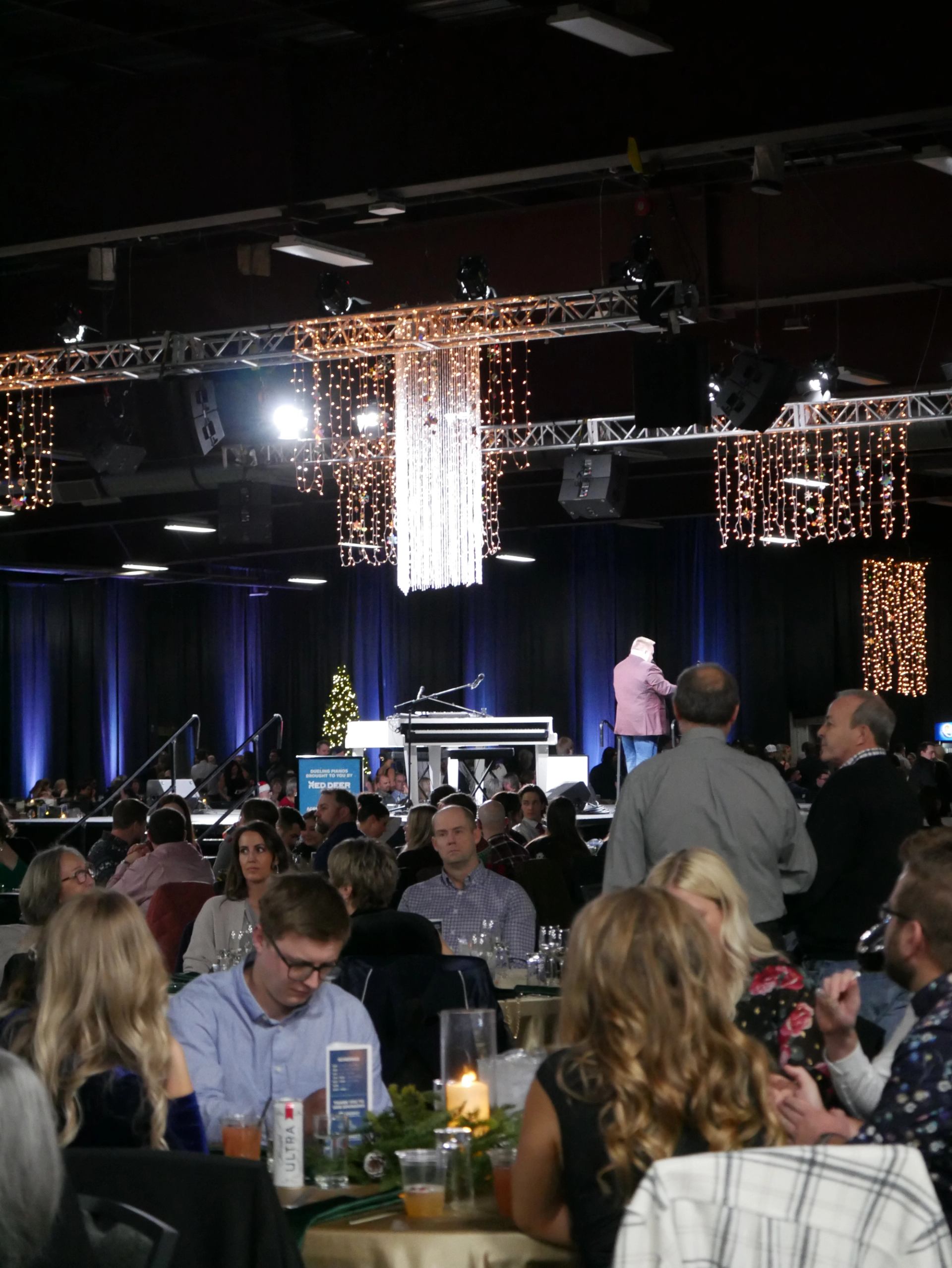 Banquet guests sit at tables facing a stage beneath hanging lights.