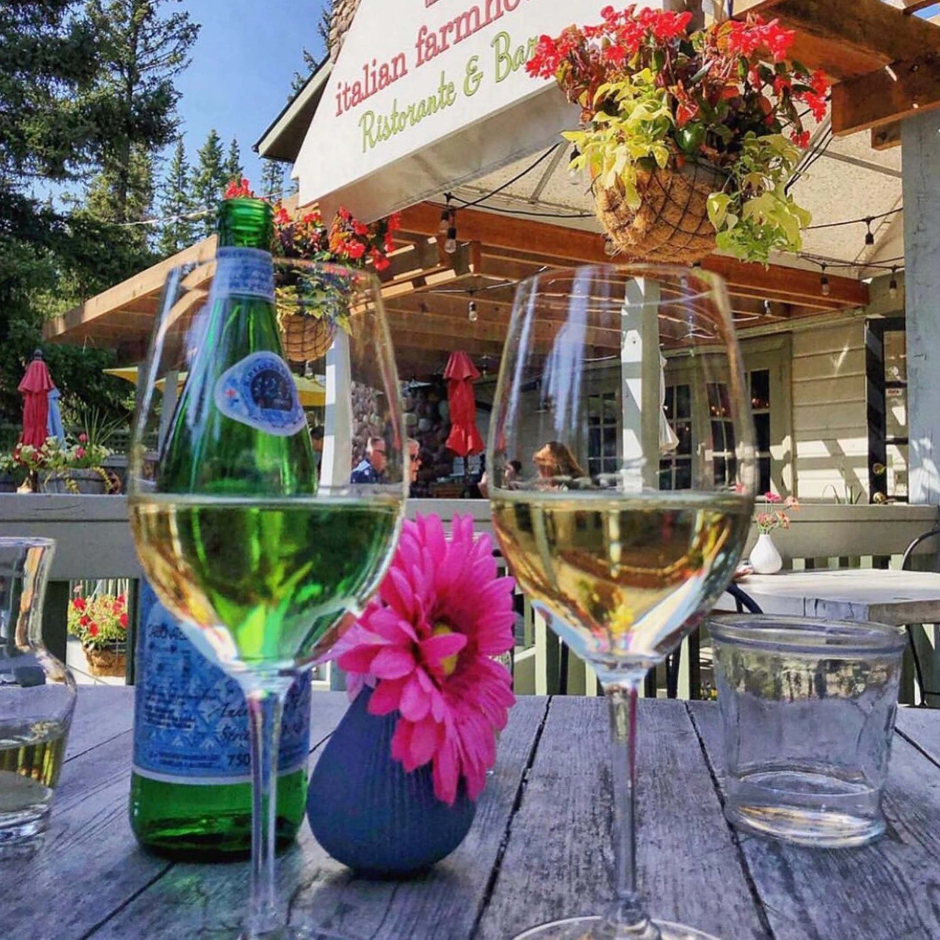 Wine glasses, water bottle and pink flowers on an Italian farmhouse restaurant patio table.