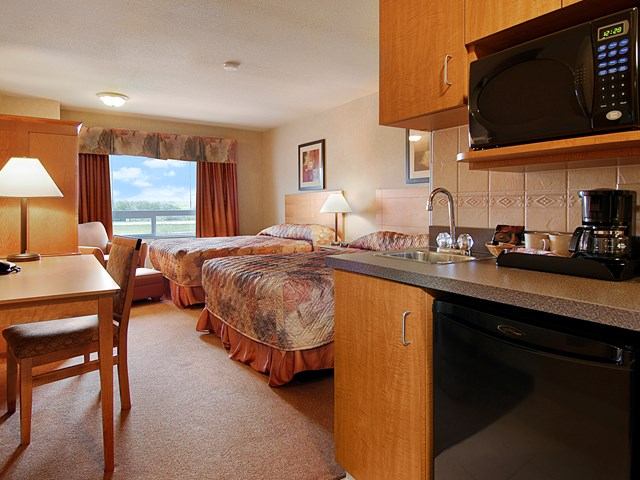 Hotel room at Canalta Provost with two beds, kitchenette, desk, and window view.