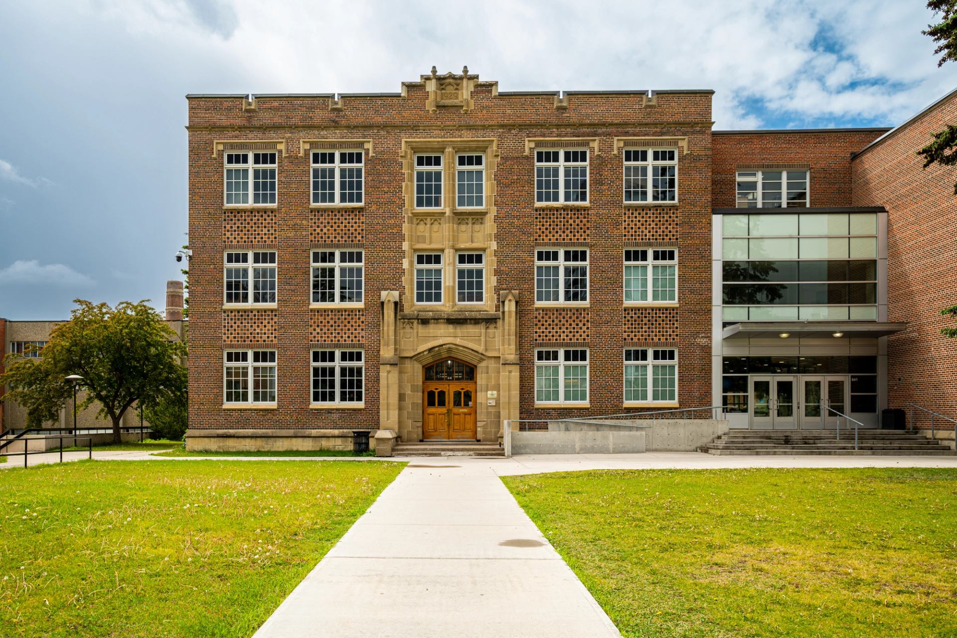 Brick school building with central arched entrance, large windows and adjacent glass extension.
