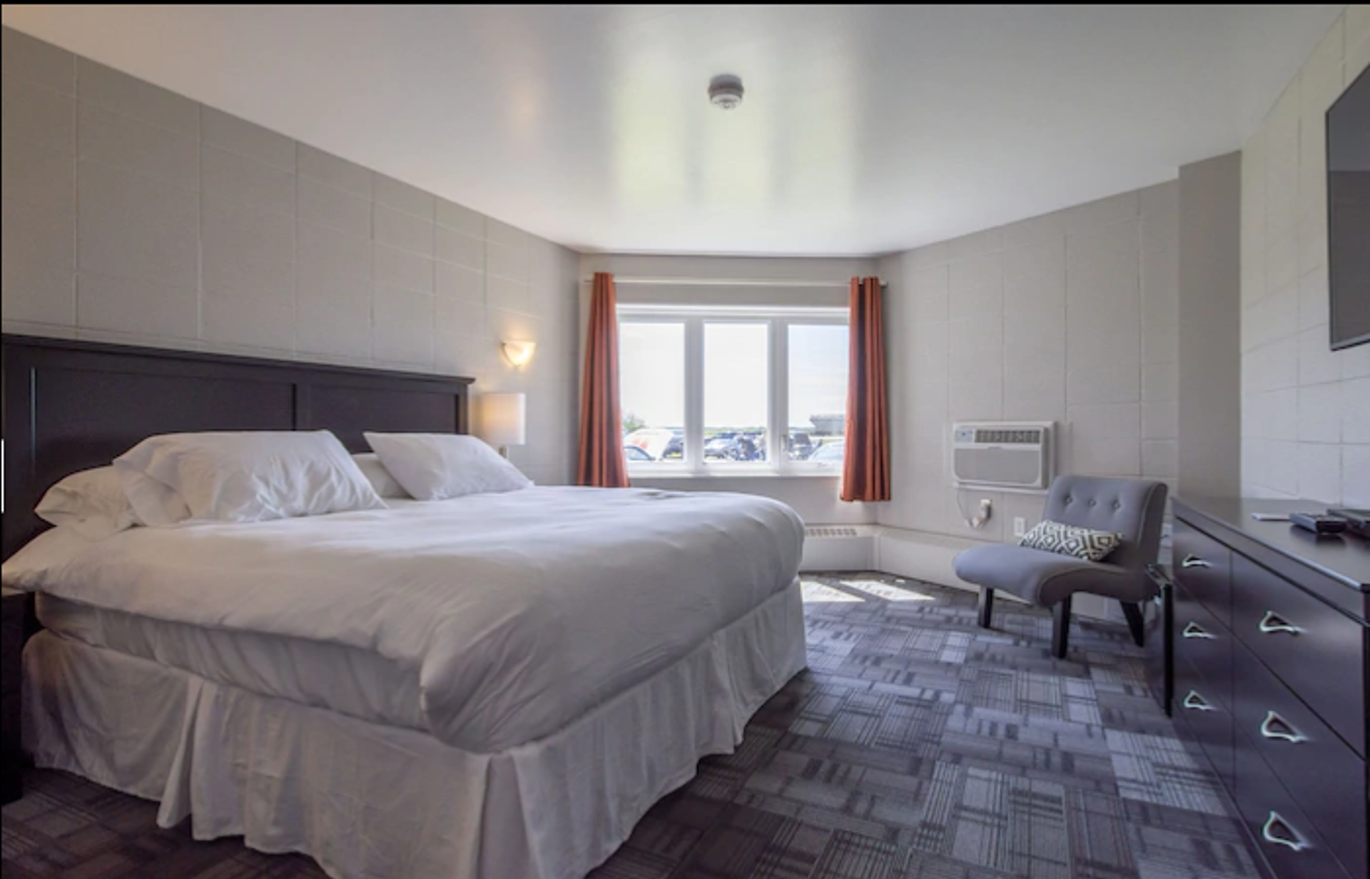 Bright room with a king bed, gray carpet, chair, and window with outdoor view
