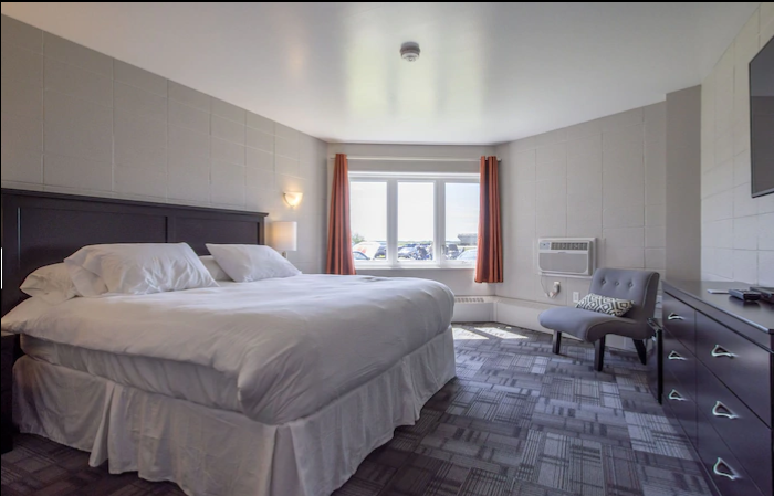 Bright room with a king bed, gray carpet, chair, and window with outdoor view