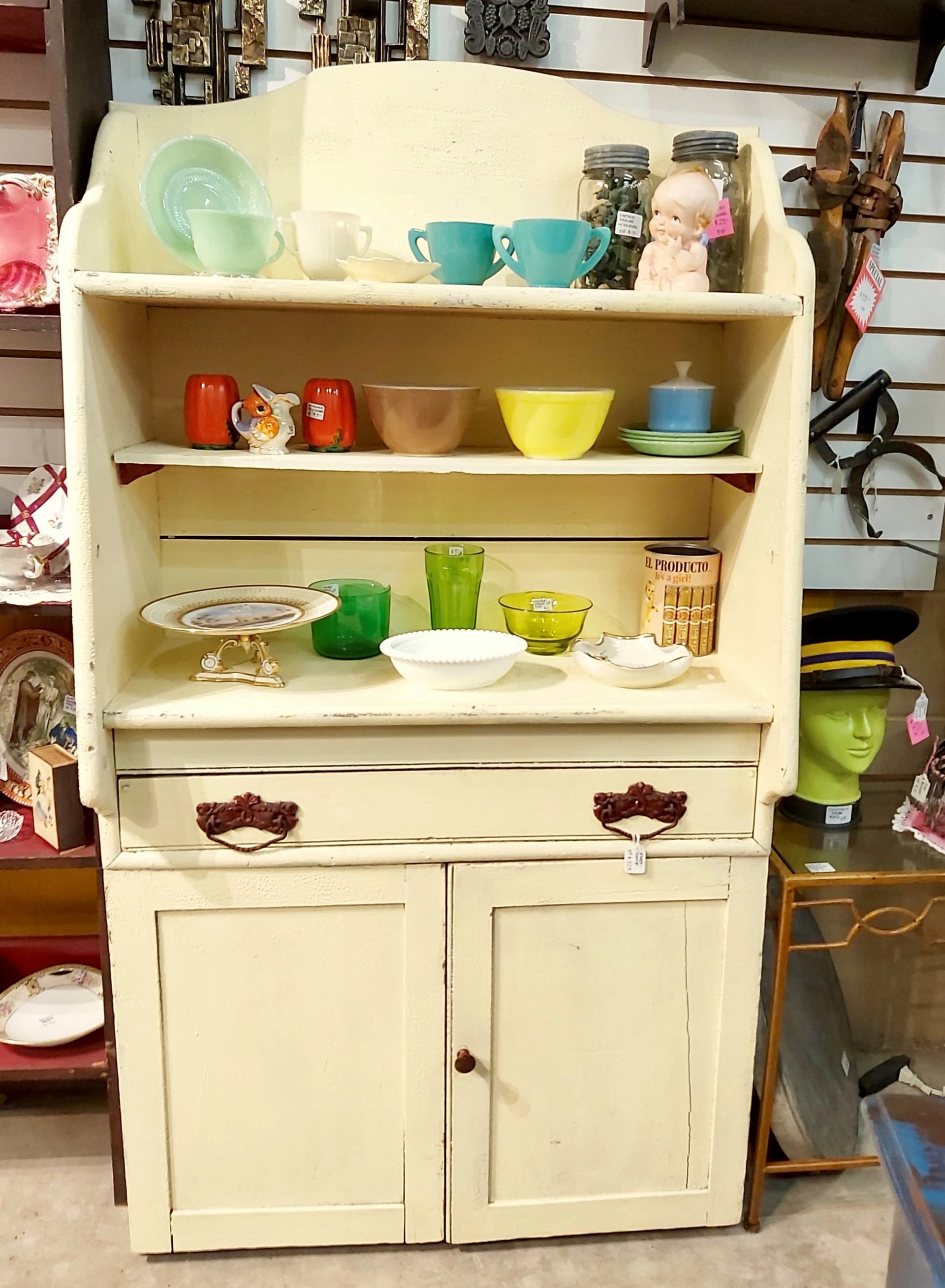 Cream vintage hutch display with colourful cups, bowls, jars and glassware.