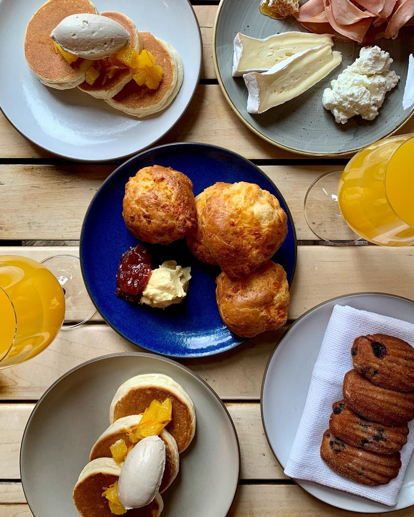 Model Milk brunch with pancakes, cheese, pastries, and orange juice on a wooden table.