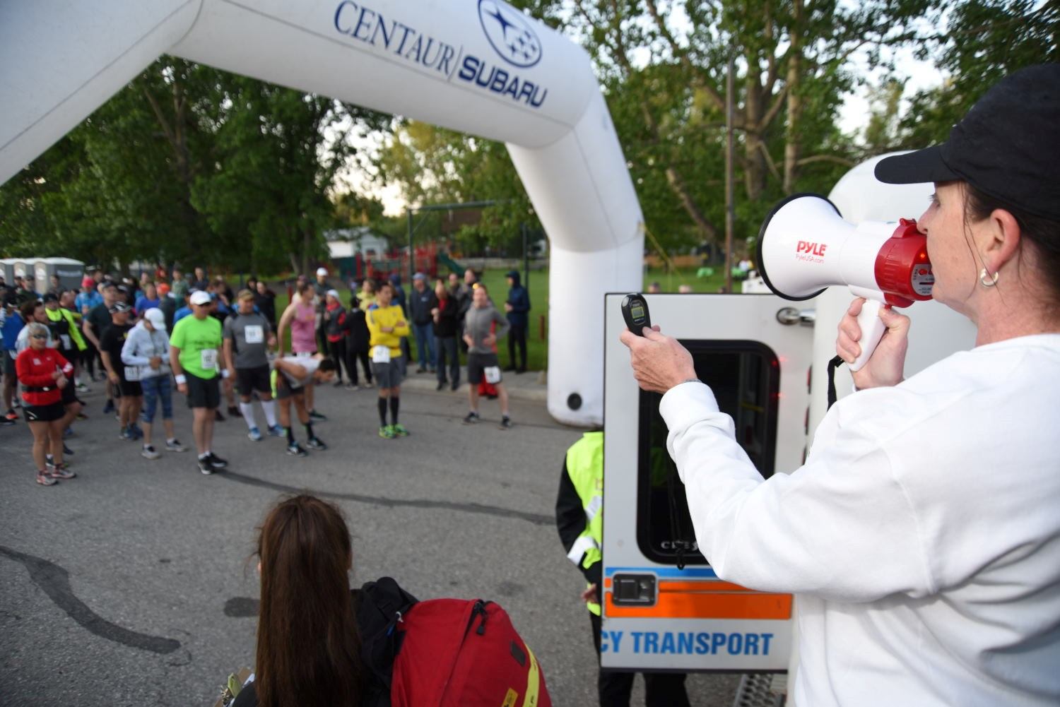 Race announcer uses a megaphone near a crowd of runners at an outdoor event.