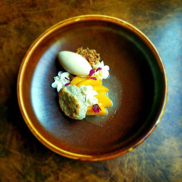 Artfully plated dessert with ice cream, fruit, crumble, and edible flowers.
