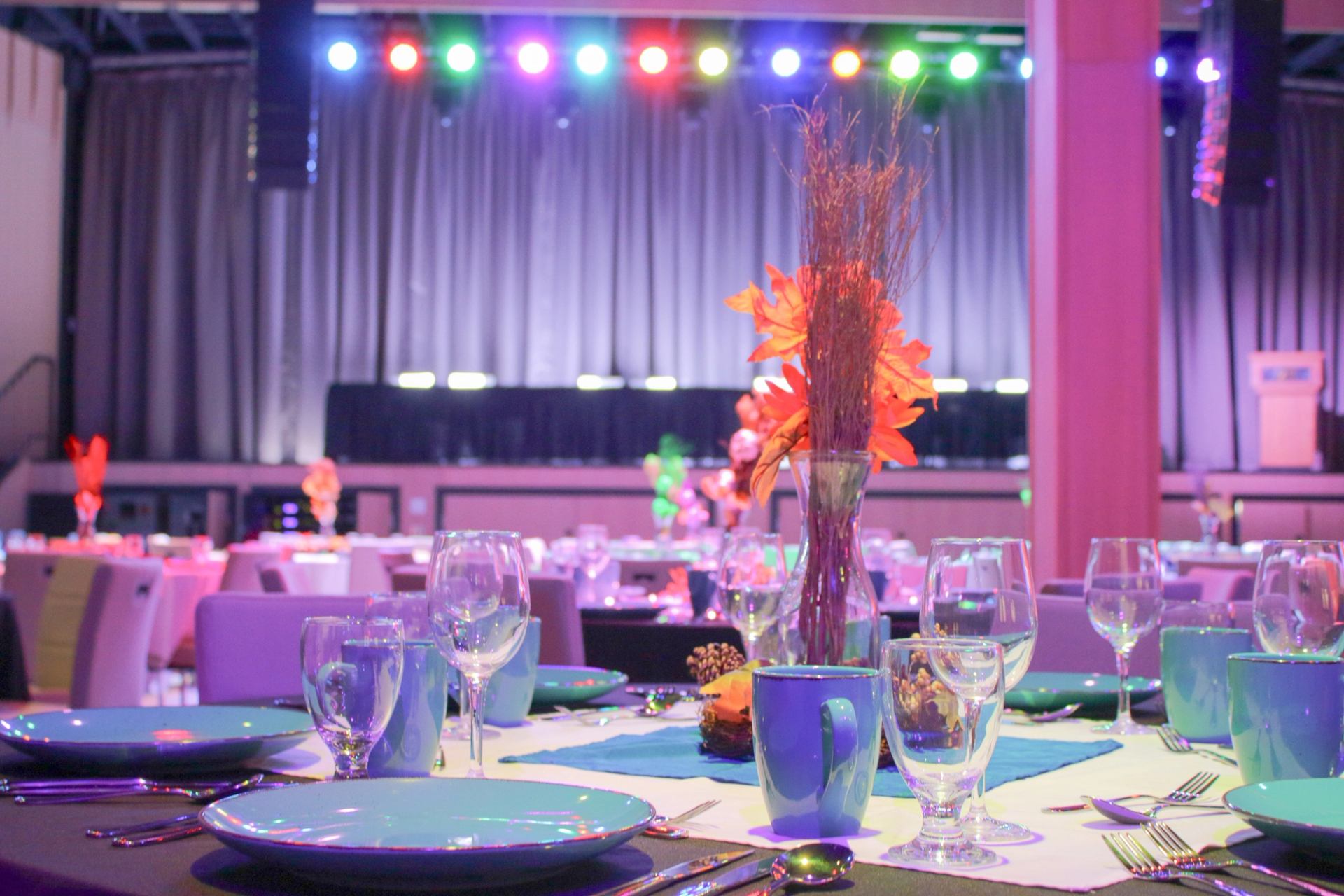 Event space with blue table settings, floral centerpieces, and stage lighting.
