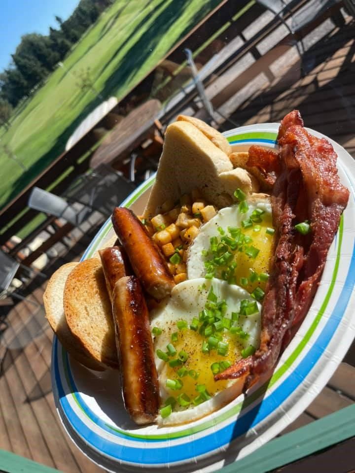 Plates of breakfast food with eggs, sausages, toast, and chopped green onions on a deck.