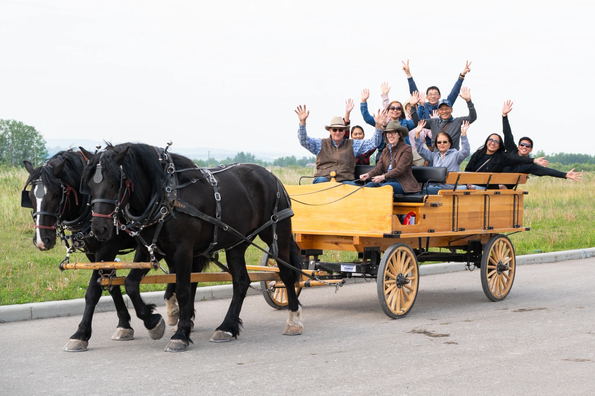 Group rides horse drawn wagon and waves while traveling along road at Stampede event.