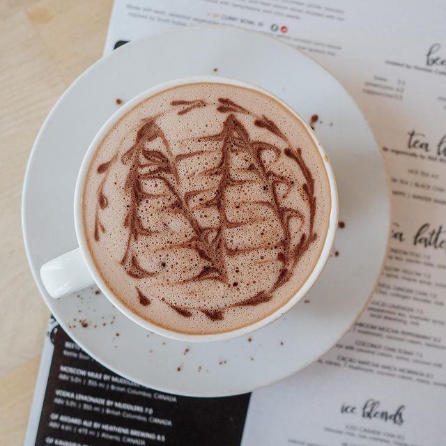 Latte with ship-shaped foam art on saucer over café menu.