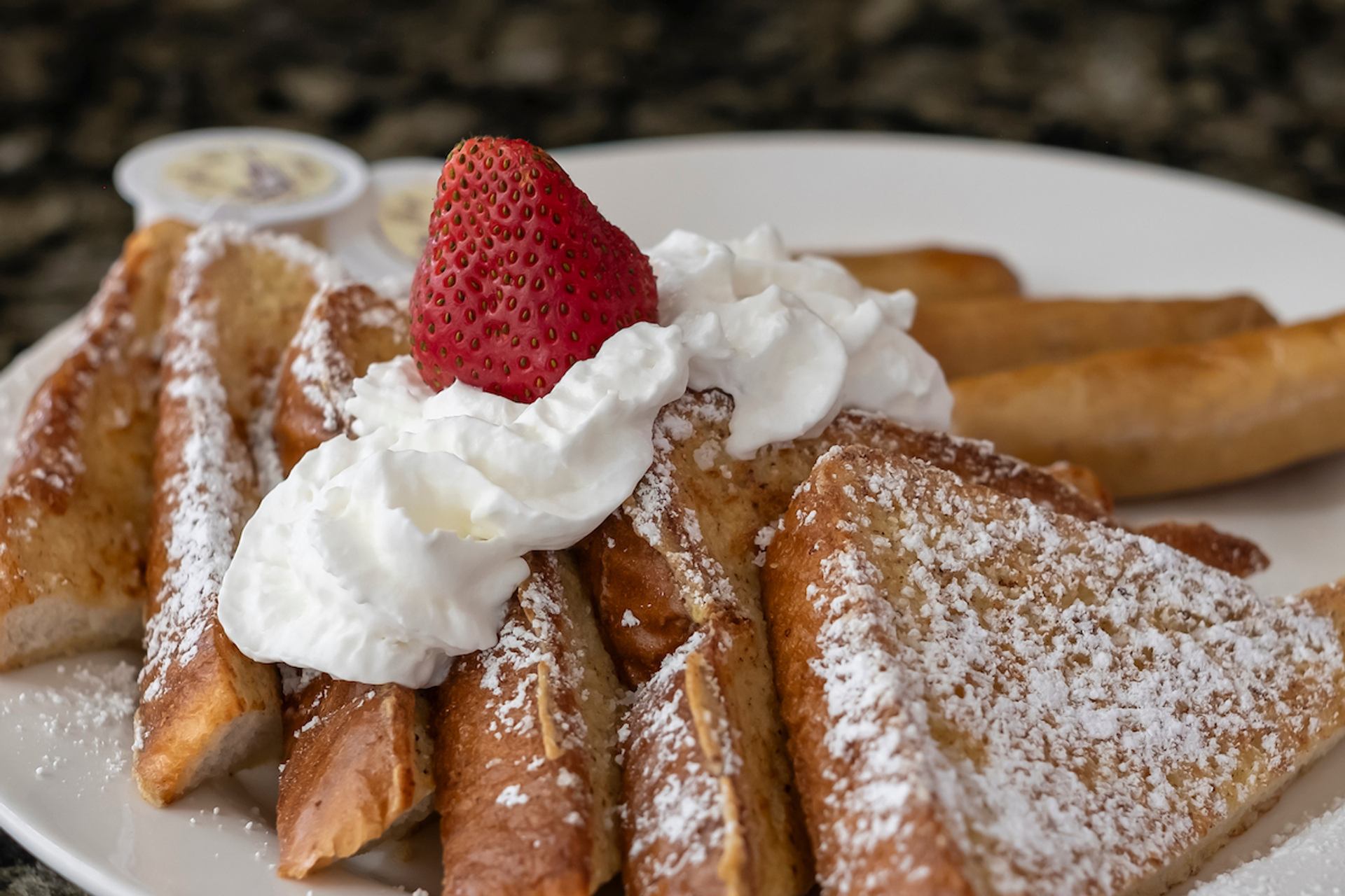 French toast slices with whipped cream, strawberry and icing sugar on white plate.