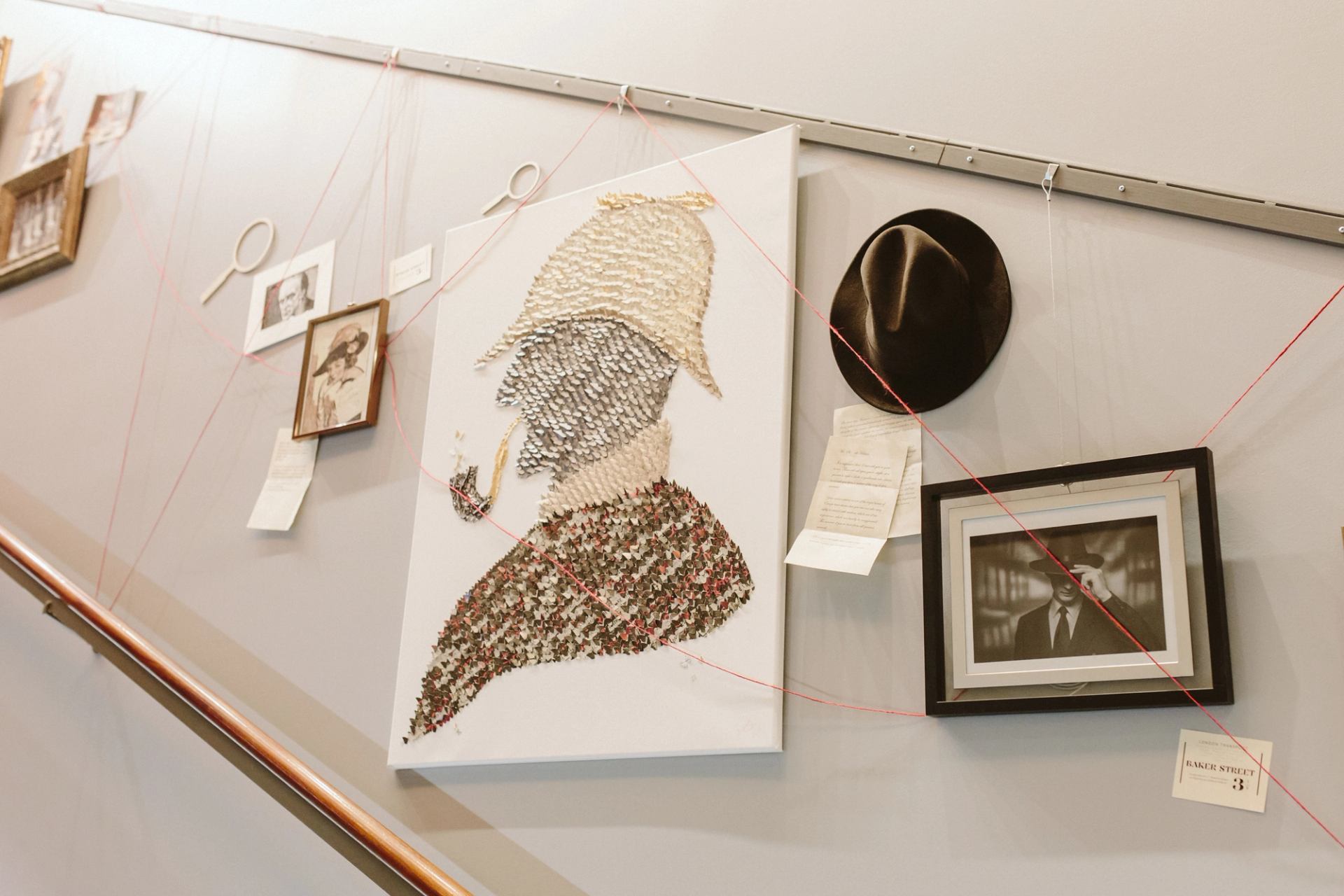 Wall display with detective silhouette artwork, hat, photos and notes linked by red string.