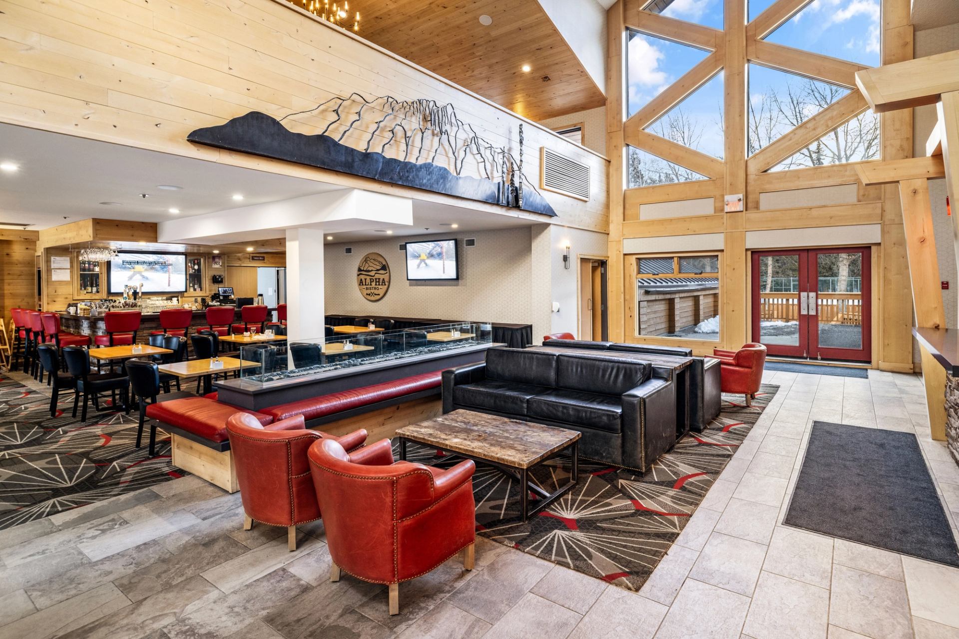 Hotel lobby with red chairs, black couches, and a restaurant in the background with red bar stools.