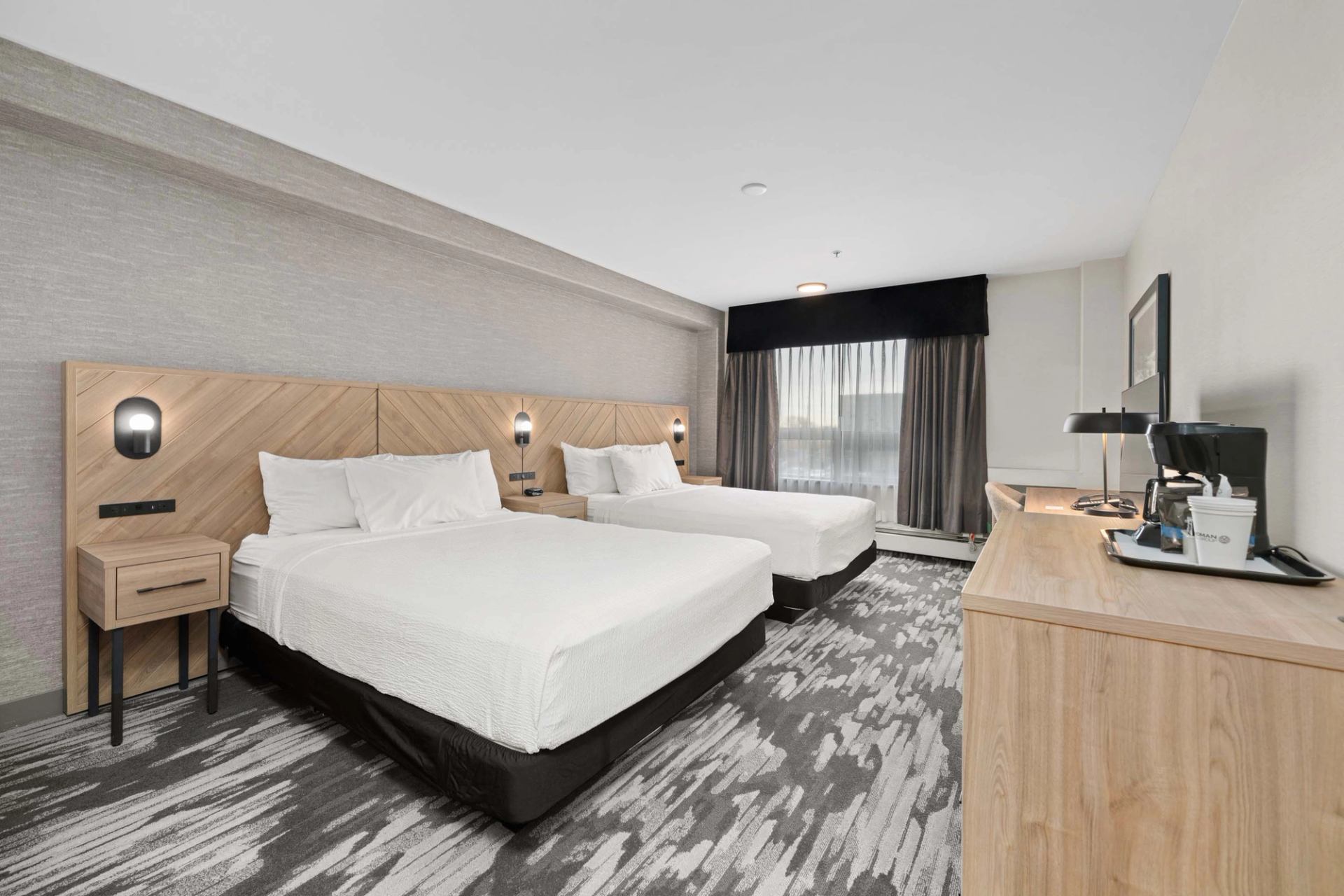 Hotel room with two beds, wood headboards, desk, coffee station and large window.