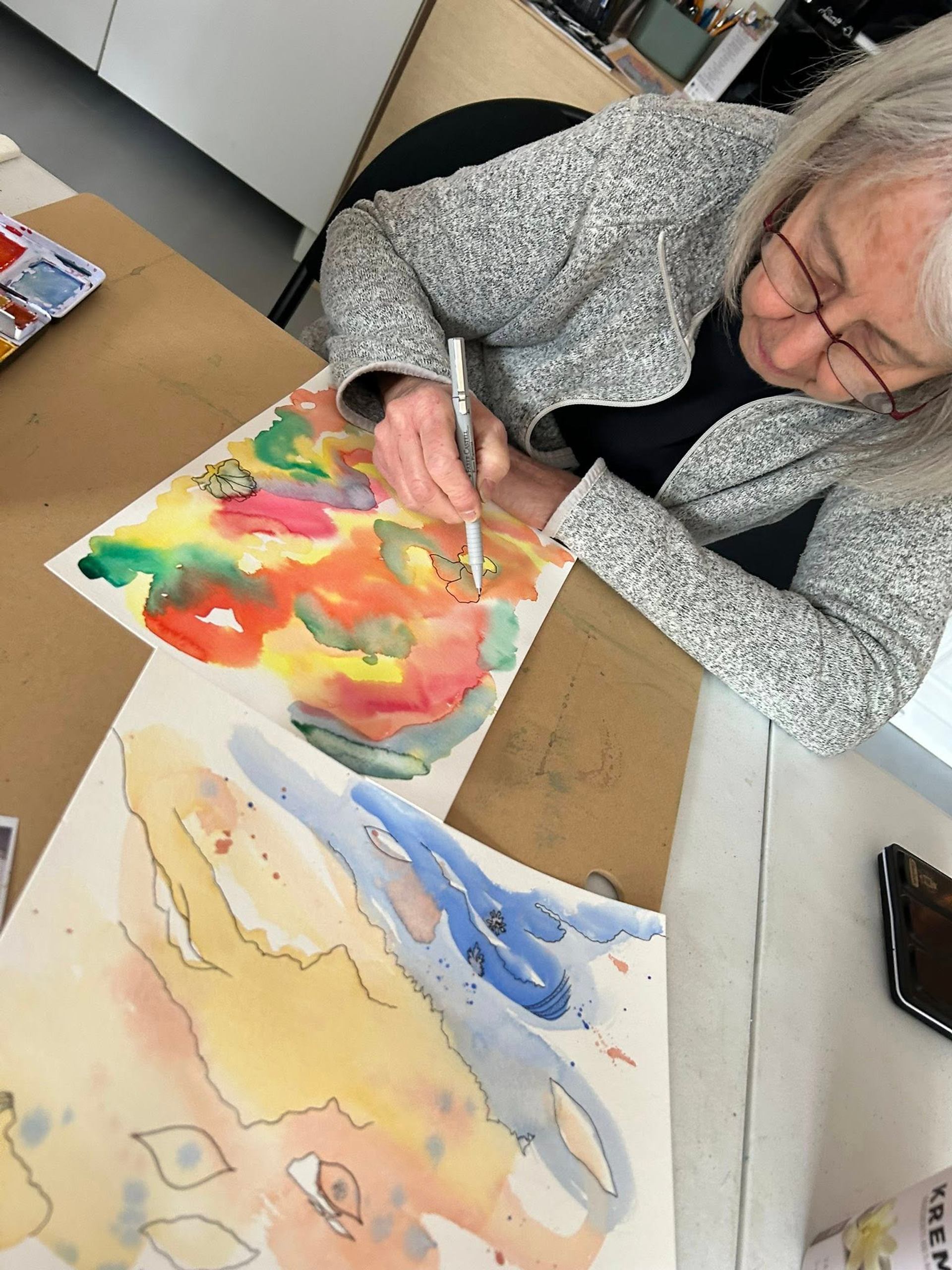 Person painting abstract art with vibrant and soft colors at a table.