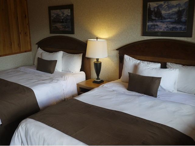 Hotel room with three beds, lamps, and framed landscape pictures on the wall.
