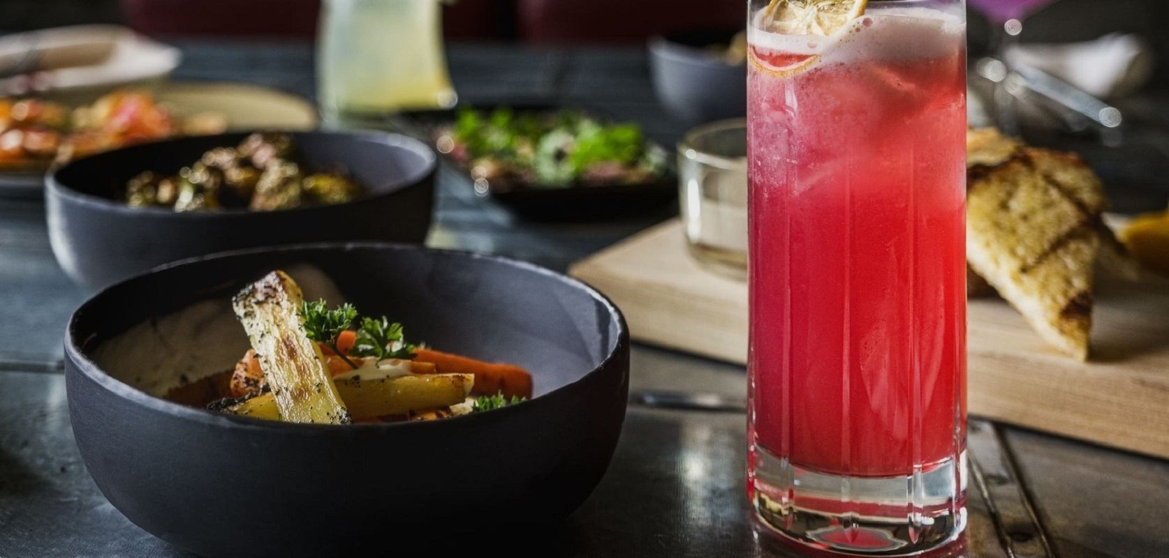 Close-up of a vibrant pink cocktail with gourmet dishes in the background.