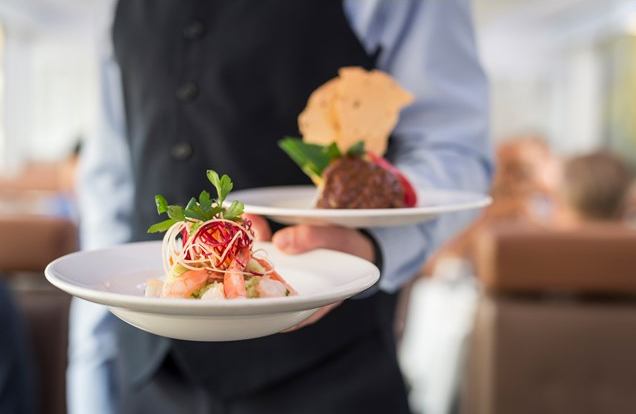 A server holds to dishes with elegantly plated food.